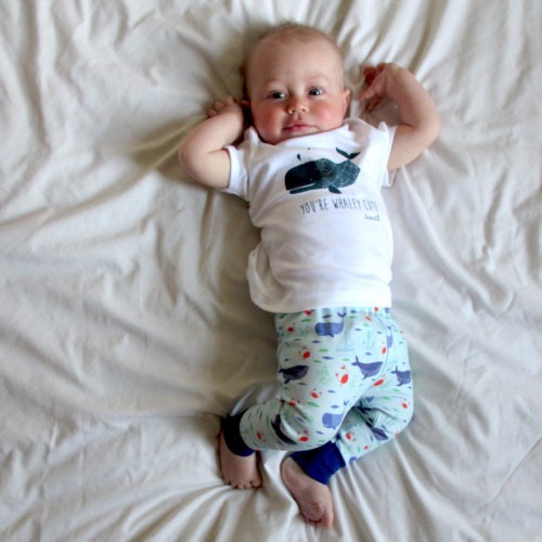 Baby wearing whale baby outfit. Blue whale baby leggings featuring whales, jelly fish and crabs and a baby T-shirt with a whale and slogan 'You're whaley cute'