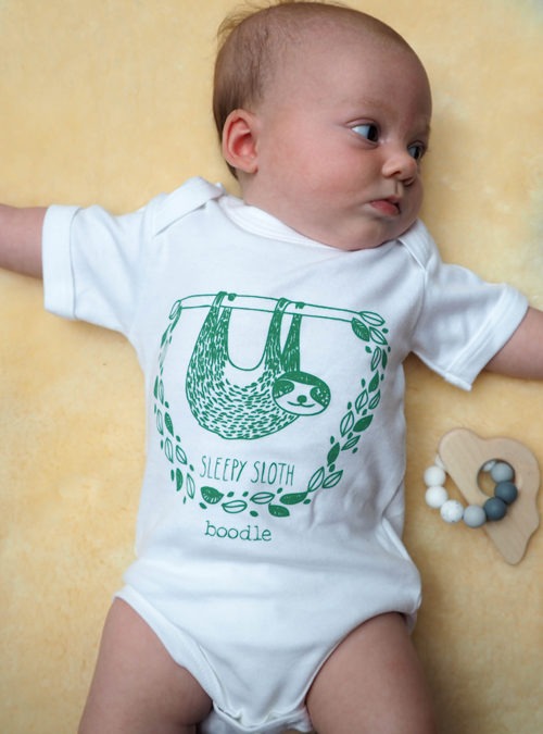 baby wearing a cute sloth white baby grow. Green print of a sloth hanging in the jungle