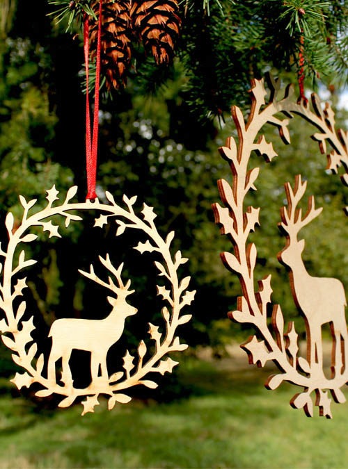Photograph of 2 deer wreaths hanging in a tree. Birch wood has been laser cut into a festive wreath featuring a deer and holly surrounding it.