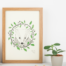 Badger and oak art print. Photo of a framed print featuring an illustration of a badger surrounded by an oak wreath. Green and black print on a natural white background.