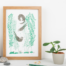 Photo of a art print featuring 3 otters playing in kelp. Screen printed by hand, the otters are brown and the kelp green. Photo is of a framed print with props such as plants and pencils surrounding it