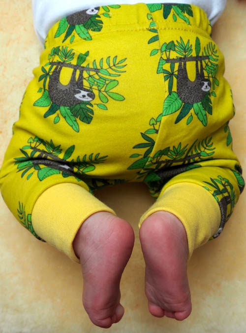 baby wearing sloth leggings. repeat pattern of a sloth hanging on a branch surrounded by leaves.