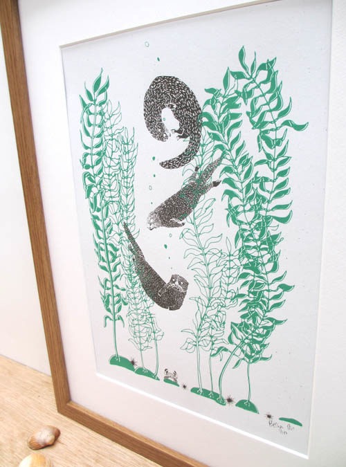 photo of a close up of an art print featuring 3 otters playing in kelp