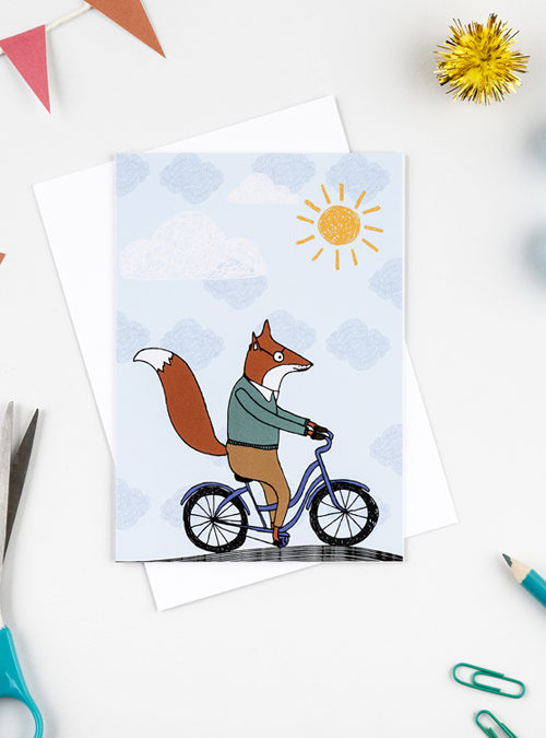 photograph of a fox card featuring a fox riding a bike in the sunshine.