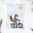 photograph of a fox card featuring a fox riding a bike in the sunshine.