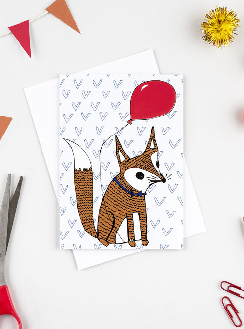 photograph of a greetings card featuring an orange fox holding a red balloon