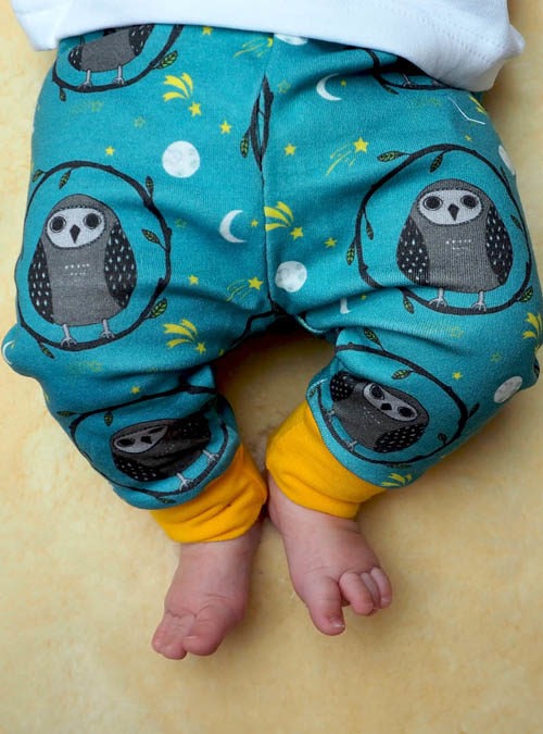 baby wearing teal owl leggings. Teal leggings with a repeat pattern of baby owls with a yellow cuff