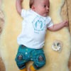 model wearing owl baby outfit. owl repeat pattern featuring cute baby owls on a perch with yellow cuffs. White organic t-shirt featuring a teal print of an owl