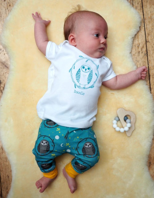 model wearing owl baby outfit. owl repeat pattern featuring cute baby owls on a perch with yellow cuffs. White organic t-shirt featuring a teal print of an owl
