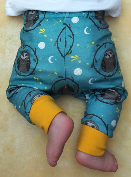 Photo of owl baby leggings from the back. Owl repeat pattern on a teal background showing how they fit on the babys bum.