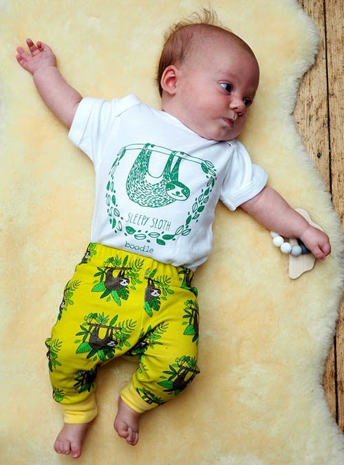 baby wearing sloth T-shirt and sloth leggings. White baby T-shirt featuring a hanging sloth along with yellow baby trousers with hanging sloths