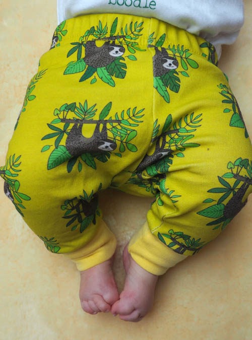Baby wearing yellow sloth baby leggings featuring hanging sloths