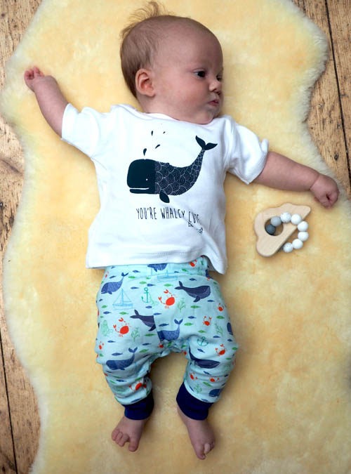 Baby lying on a sheep skin rug wearing organic cotton whale T-shirt and leggings.