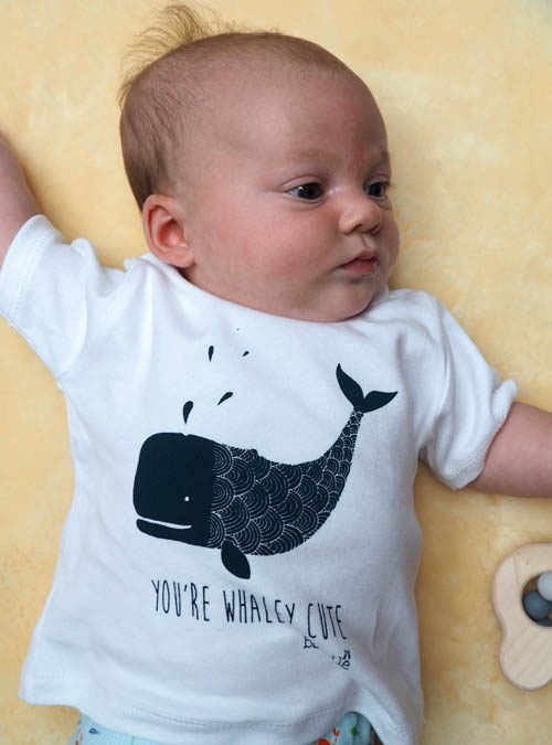 New born babu wearing white organic cotton T-shirt featuring a whale with the wording 'You're whaley cute' underneath