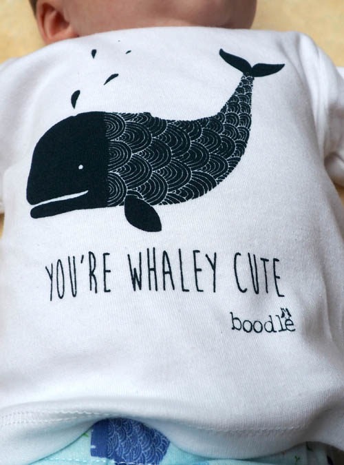 Baby model wearing a organic cotton T-shirt featuring a picture of a whale with 'You're whaley cute' underneath