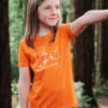 Kid model wearing an orange T-shirt featuring foxes on a camping trip with the text 'Lets go on an adventure' underneath