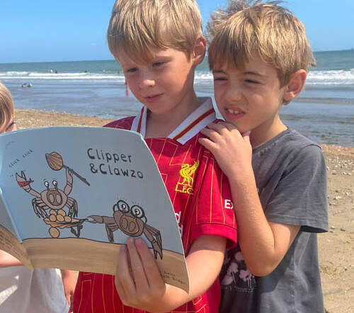3 boys reading Clipper and Clawzo on the beach