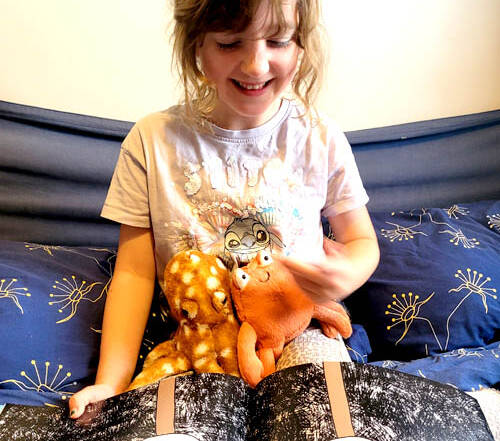 Child reading Clipper and Clawzo holding 2 cuddly toys