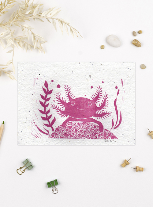 photograph of a axolotl lino print surrounded by little props like pebbles, clips and natural grasses