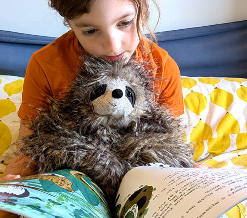Kid reading Sloth moth book holding a cuddly sloth