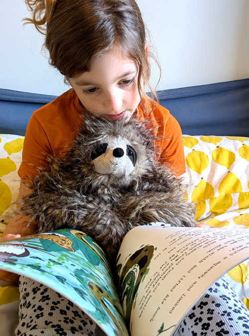 Kid reading Sloth moth book holding a cuddly sloth